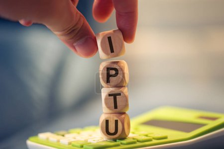 Photo for Close-up view of man forming acronym IPTU with wooden cubes. A calculator in the composition. - Royalty Free Image