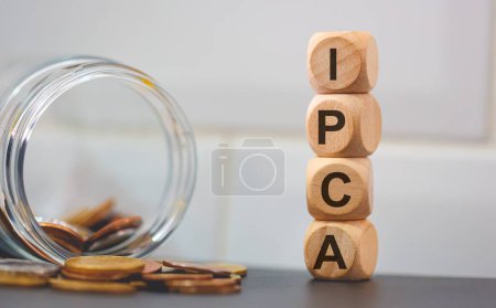 Foto de Acrónimo IPCA para el Índice Nacional Amplio de Precios al Consumidor escrito en cubos de madera y pilas de monedas. Estudio foto. - Imagen libre de derechos