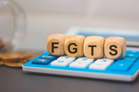 Téléchargez les photos : L'acronyme FGTS écrit sur des cubes de bois. Une calculatrice dans la composition. - en image libre de droit