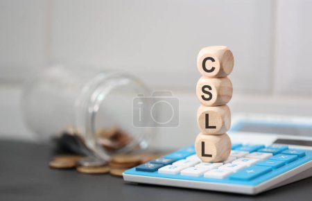 Téléchargez les photos : L'acronyme CSLL écrit sur des cubes de bois. Une calculatrice dans la composition. - en image libre de droit