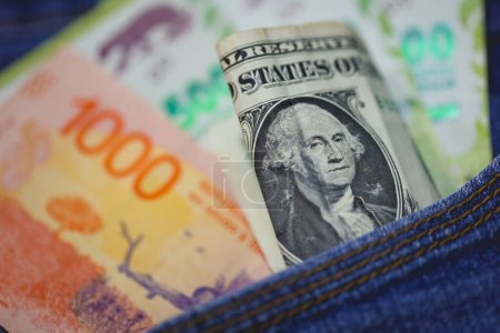 Argentine peso banknotes and United States dollar bills in a jeans pocket in macro photo.