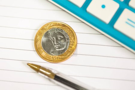 Foto de Moneda brasileña, pluma y calculadora sobre fondo de cuaderno - Imagen libre de derechos