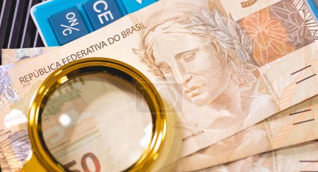 Téléchargez les photos : Billets Real brésilien et verre grossissant doré Économie, finances et impôt sur le revenu brésiliens. - en image libre de droit