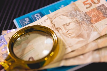 Foto de Billetes reales brasileños y lupa dorada.Economía, finanzas e impuestos sobre la renta brasileños. - Imagen libre de derechos