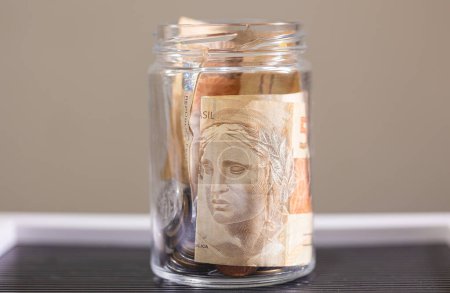 Téléchargez les photos : Real brésilien billets à l'intérieur d'une tirelire de pièces en verre pot. - en image libre de droit