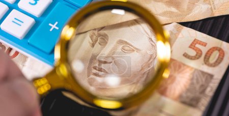 Brazilian Real banknotes and a golden magnifying glass.Brazilian economy, finance and income tax.