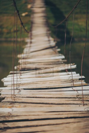 Stary most wiszący ciągnący się nad rzeką. Stary długi wiszący drewniany kładka nad rzeką. most W potrzebie naprawy, często używane przez podróżnych, niebezpieczne do przekroczenia, na odległym obszarze wiejskim.