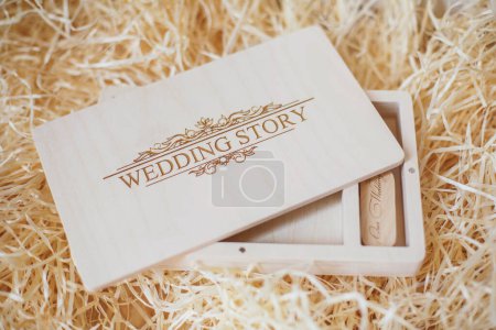 Photo for Wooden photo box for photo storage on straw background. Open Box with flash with laser engraving "wedding story" set for the photographer, presentable set of photos, luxury feedback to client. - Royalty Free Image