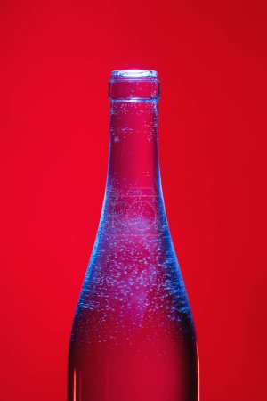 Ausschnitt aus einer Flasche Rosenchampagner mit Blasen auf blauem Licht auf rotem Hintergrund. Flasche mit Soda. 