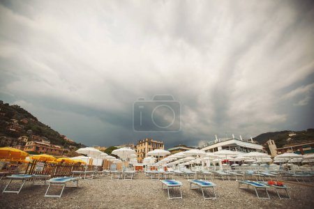 The empty beach before a rain. Mediterranean coast, empty sun beds, umbrellas from the sun, mountains, pebbles. Beach umbrellas at the hotel lounge chairs. beach sea sky before a thunderstorm, travel.