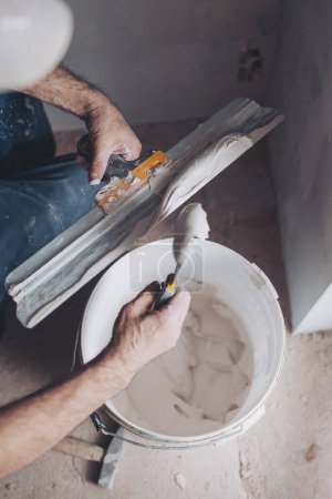 Travailleur met du mastic sur une spatule pour plâtrer les murs intérieurs dans un salon. plâtre travaux plâtrage deux truelles placoplâtre.