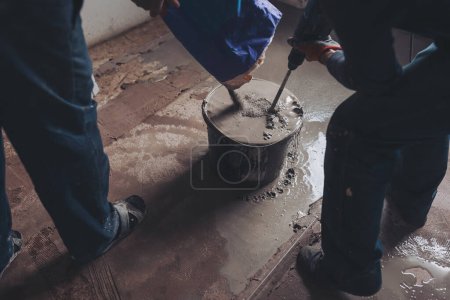 Workers put dry plaster into a bucket. Workers mixing concrete in bucket indoors. A professional craftsman kneads mortar in a bucket with a mixer - adhesive mortar for bricks. 