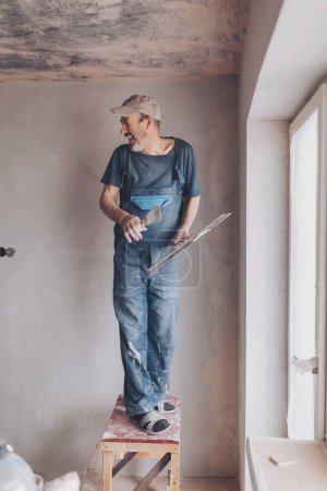 Laughing Male builder, master office, plasterer with a tool in working clothes. Home improvement, spackling. 