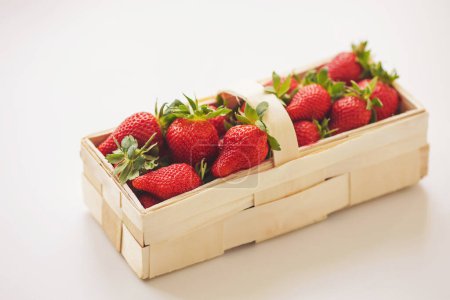 Fresas en una cesta de madera y sobre un fondo blanco. Fresas frescas jugosas. 