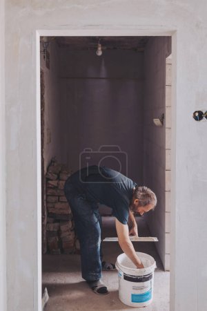 Plasterer covering a stained damp patch in a white wall with new plaster or masonry during renovations or maintenance on a house interior