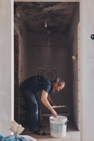 Plasterer covering a stained damp patch in a white wall with new plaster or masonry during renovations or maintenance on a house interior