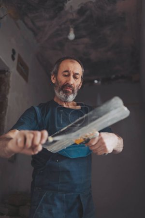 Senior man working with spatula and plaster while renovating interior , makes repairs in the house. 