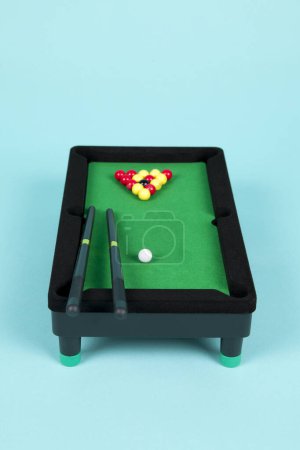 Téléchargez les photos : Une table de billard en plastique miniature sur fond turquoise, avec triangle, repères et boules - en image libre de droit