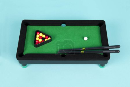 Foto de Una mesa de billar de plástico en miniatura sobre un fondo turquesa, completa con triángulo, señales y bolas - Imagen libre de derechos