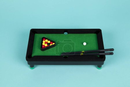 Photo for A miniature plastic billiard table on a turquoise background, complete with triangle, cues and balls - Royalty Free Image