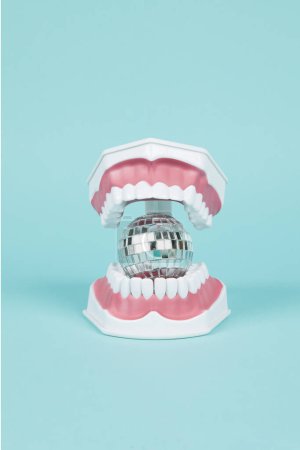 Foto de Una dentadura plástica con una bola discoteca en la boca sobre un fondo turquesa. Fotografía de bodegón de color mínimo y creativo - Imagen libre de derechos
