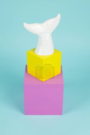 Téléchargez les photos : Une queue de sirène en céramique irisée sur une pile de cubes roses et jaunes. Fond turquoise. Photographie de natures mortes minimale et créative - en image libre de droit
