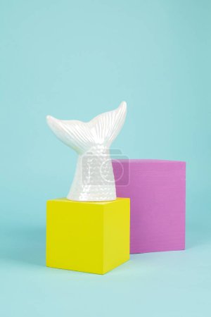 Foto de Una cola de sirena en cerámica iridiscente sobre una pila de cubos rosados y amarillos. Fondo turquesa. Fotografía de bodegón mínima y creativa - Imagen libre de derechos