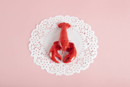 Téléchargez les photos : Un homard en métal rouge sur fond blanc napperon et rose. Photographie minime couleur nature morte - en image libre de droit