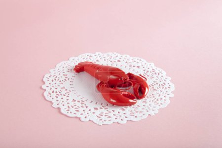 Photo for A red metal lobster on a white doily and pink background. Minimal color still life photography - Royalty Free Image