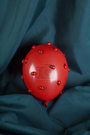 Foto de Una invasión de numerosas mariquitas en un globo inflable rojo con un fondo de cortina verde. Fotografía de bodegón de color mínimo. - Imagen libre de derechos