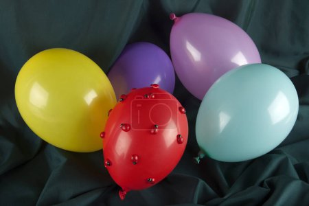 Téléchargez les photos : Un ballon rouge recouvert de coccinelles parmi les ballons dans des couleurs harmonieuses sur un fond vert ondulé. Photographie minime couleur nature morte. - en image libre de droit