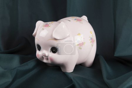 Photo for A vintage piggy bank in pink with flower designs on a wavy green curtain background. cute. Minimal color still life photography. - Royalty Free Image