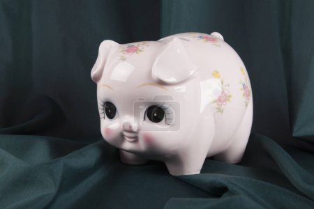 Photo for A vintage piggy bank in pink with flower designs on a wavy green curtain background. cute. Minimal color still life photography. - Royalty Free Image
