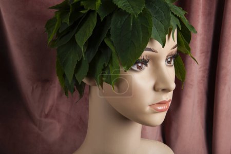 Photo for A display mannequin wearing hair of leaves and representing a nature goddess in front of a pink velvet curtain. Minimal color still life photography. - Royalty Free Image