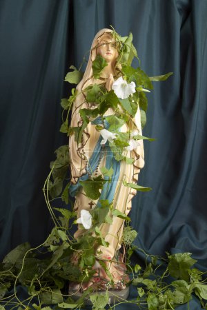 Foto de Una estatuilla de la Virgen María cubierta de bindweed delante de una cortina verde ondulado. una metáfora del tiempo y su poesía. Fotografía mínima de naturaleza muerta - Imagen libre de derechos