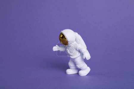 Photo for An astronaut figurine in a spacesuit exploring a plain purple background. Minimal creative still life colourful photography - Royalty Free Image