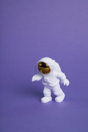 Photo for An astronaut figurine in a spacesuit exploring a plain purple background. Minimal creative still life colourful photography - Royalty Free Image