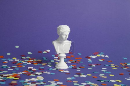 Téléchargez les photos : Un buste blanc d'une déesse sur fond violet et un tapis de confettis. Minimale couleur tendance photographie nature morte. - en image libre de droit