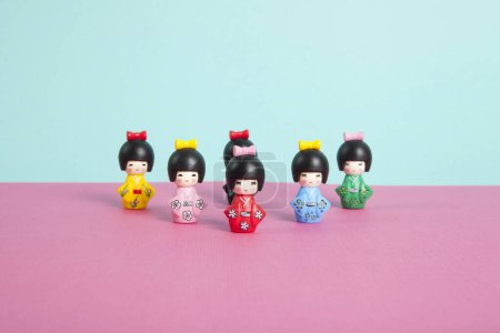 Téléchargez les photos : Une collection de poupées kokeshi en bois disposées en triangle comme des quilles de bowling sur un fond rose et bleu bicolore formant un horizon. Photographie de nature morte minimaliste et tendance. - en image libre de droit