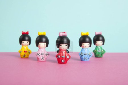 Photo for A collection of wooden kokeshi dolls arranged in a triangle like bowling skittles on a two-tone pink and blue background forming a horizon. Minimalist, trendy still life photography. - Royalty Free Image