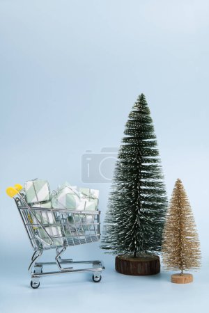 Foto de Conjunto con un caddie lleno de regalos sobre un fondo azul cielo luminoso, así como árboles de Navidad de oro y verde. Minimalista, fotografía bodegón de moda. - Imagen libre de derechos
