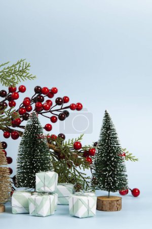 Foto de Composición con coloridos regalos, una rama de acebo con sus bayas rojas y árbol de Navidad sobre un fondo azul cielo luminoso. Minimalista, fotografía bodegón de moda. - Imagen libre de derechos