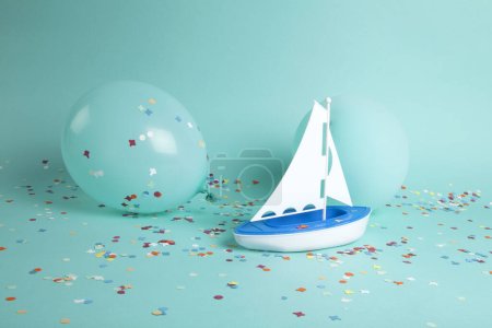 Téléchargez les photos : Un voilier naviguant sur une mer de confettis parmi des ballons iceberg. La composition est dans une palette de couleurs vert turquoise. Photographie de nature morte minimaliste et tendance. - en image libre de droit