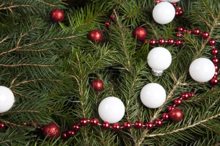 Téléchargez les photos : Zoom sur un tas de branches de sapin avec un cadre de guirlande de perles rouge vif et de nombreux Noël boule rouge et blanc. Texture pour ressource graphique - en image libre de droit