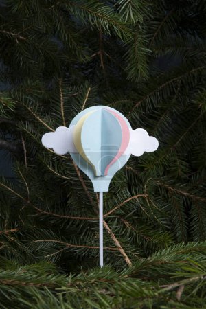 Téléchargez les photos : Un ballon en papier à air chaud, initialement une décoration de gâteau, volant depuis une forêt de sapins. Illustration poétique de la liberté - en image libre de droit