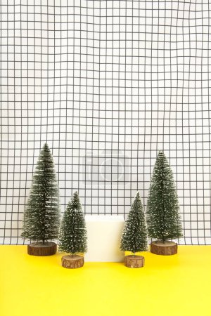 Foto de Un cubo de madera blanco rodeado de varios árboles de Navidad en miniatura sobre un fondo de rejilla en blanco y negro. soporte de exhibición de objetos vacíos. Fotografía mínima de naturaleza muerta - Imagen libre de derechos