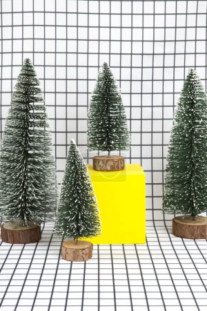 Téléchargez les photos : Une scène de forêt miniature composée de plusieurs petits arbres de Noël et d'un cube jaune sur fond de grille graphique noir et blanc. photographie de nature morte minimale - en image libre de droit