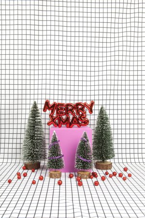 Foto de Un adorno de Navidad de plástico rojo brillante con un texto que dice feliz Navidad con adornos de navidad rojos y una escena de bosque en miniatura compuesta por varios árboles de navidad pequeños y un cubo amarillo sobre un fondo gráfico de rejilla en blanco y negro. mínimo todavía - Imagen libre de derechos