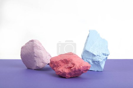 Téléchargez les photos : 3 pierres à peindre ou cailloux dans des tons rose, saumon et pastel bleu isolés sur fond blanc et violet. Nature morte minimale et photographie dynamique - en image libre de droit