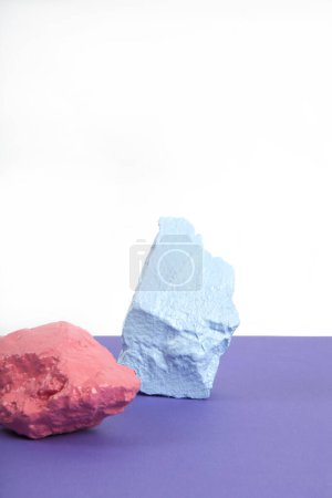 Téléchargez les photos : 3 pierres à peindre ou cailloux dans des tons rose, saumon et pastel bleu isolés sur fond blanc et violet. Nature morte minimale et photographie dynamique - en image libre de droit